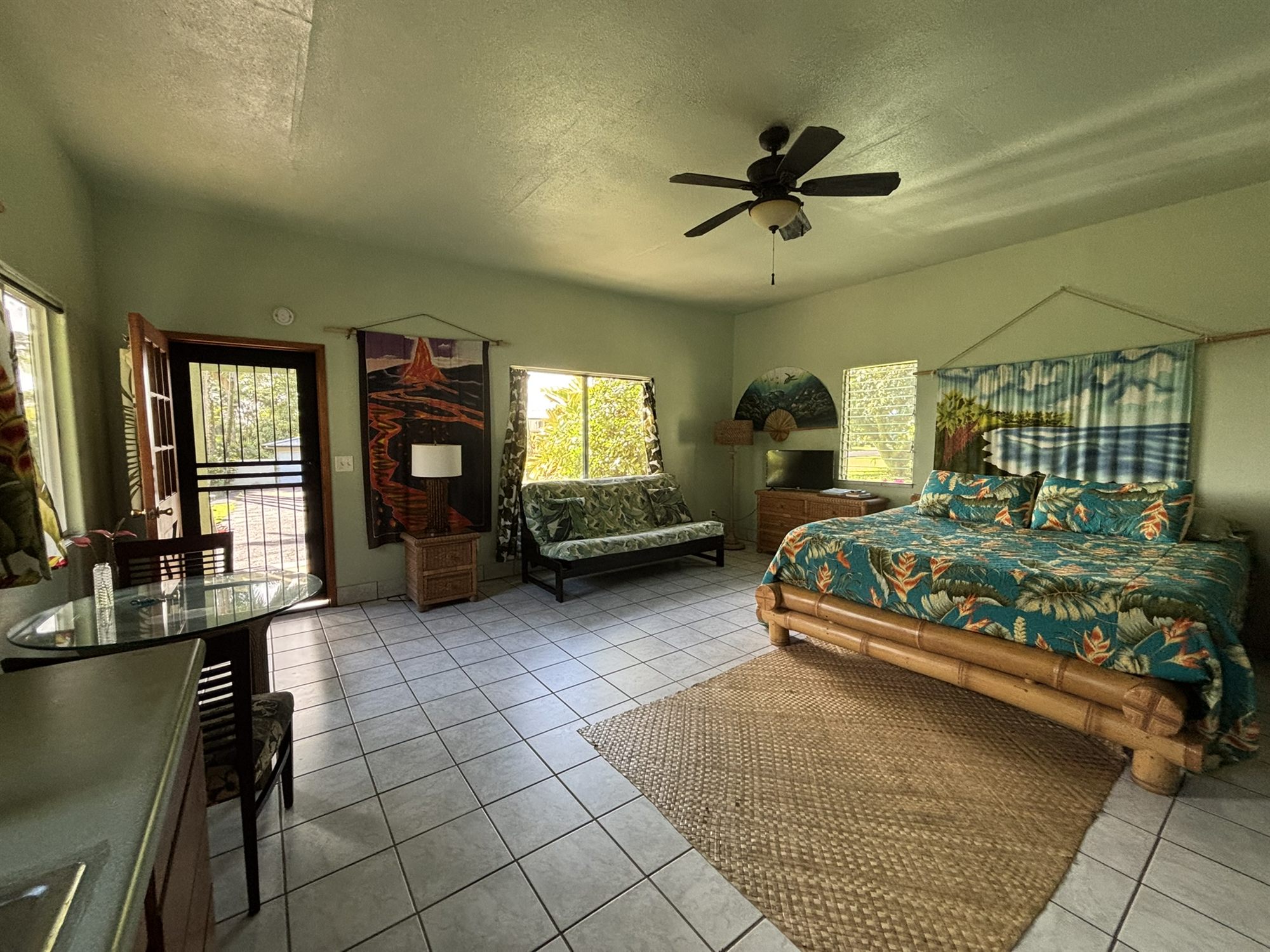 Inside the studio: bamboo king bed with a tropical quilt, futon, ceiling fan, and garden windows